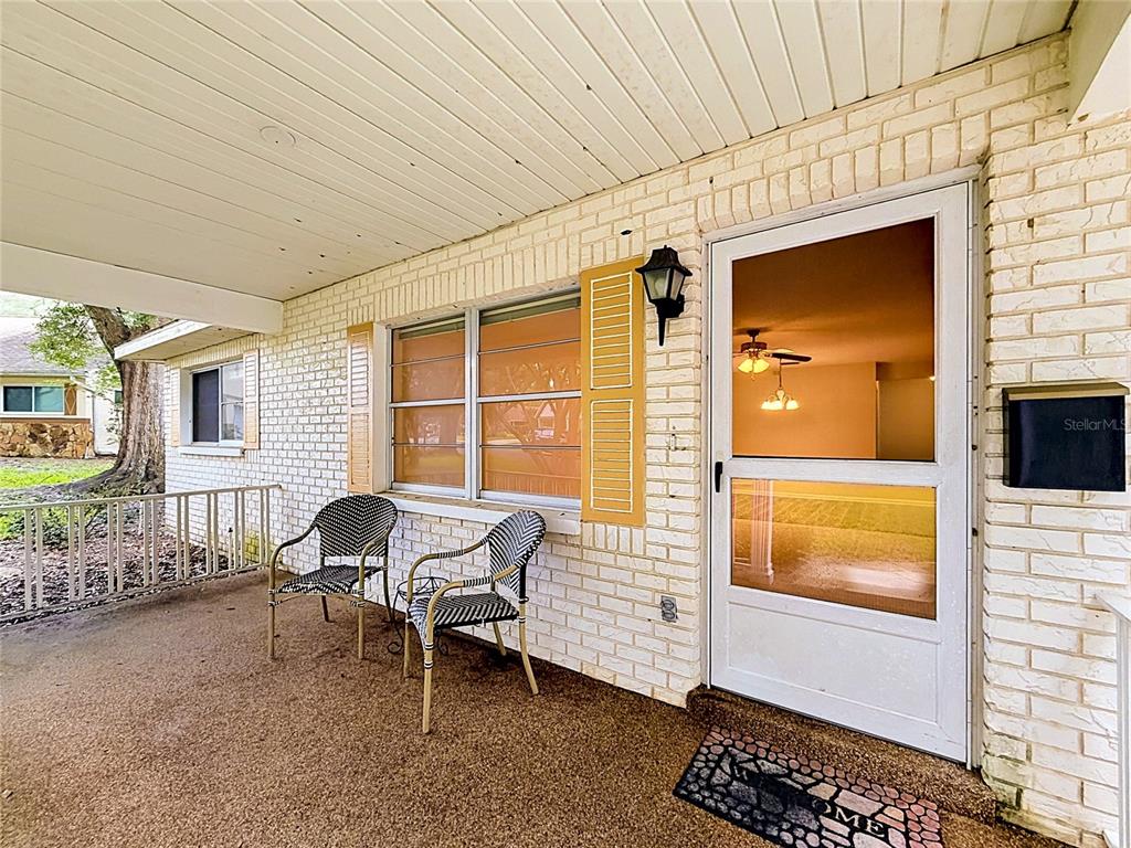 A covered front porch features white brick walls, two metal chairs, and a storm door — 9277 SW 83RD AVENUE UNIT A, OCALA, FL