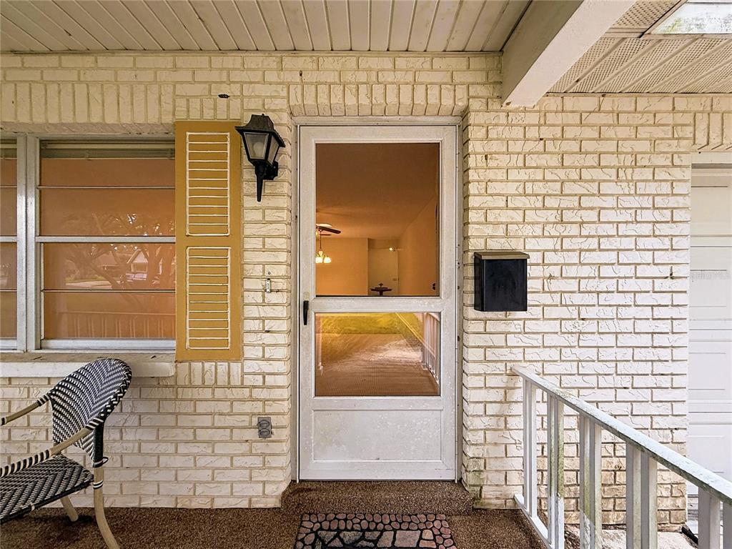 A white brick exterior features a storm door, a yellow shutter, and a porch chair — 9277 SW 83RD AVENUE UNIT A, OCALA, FL