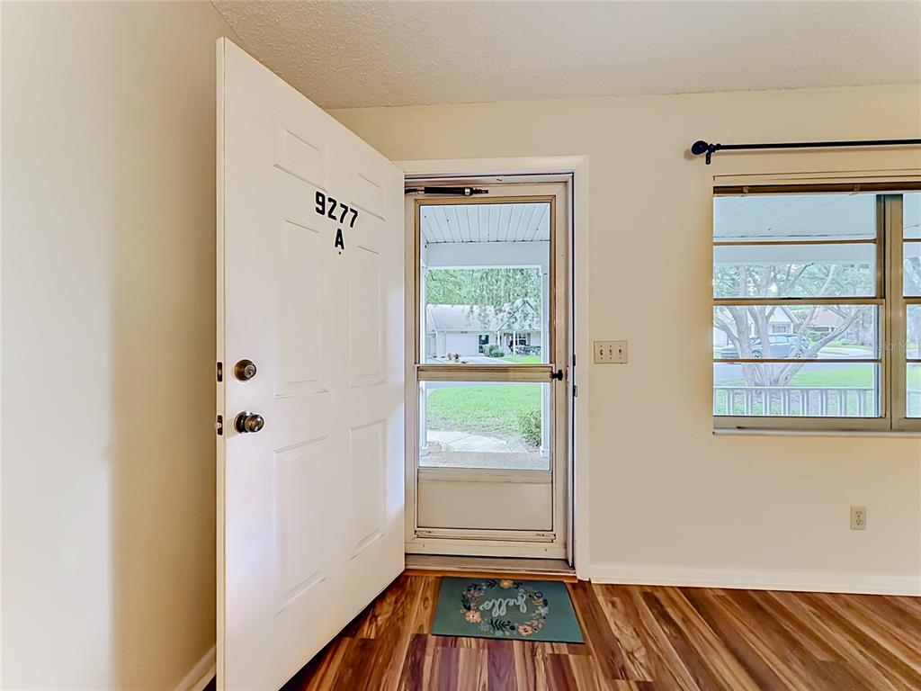 An open front door reveals a screen door, a welcome mat, and a residential neighborhood — 9277 SW 83RD AVENUE UNIT A, OCALA, FL
