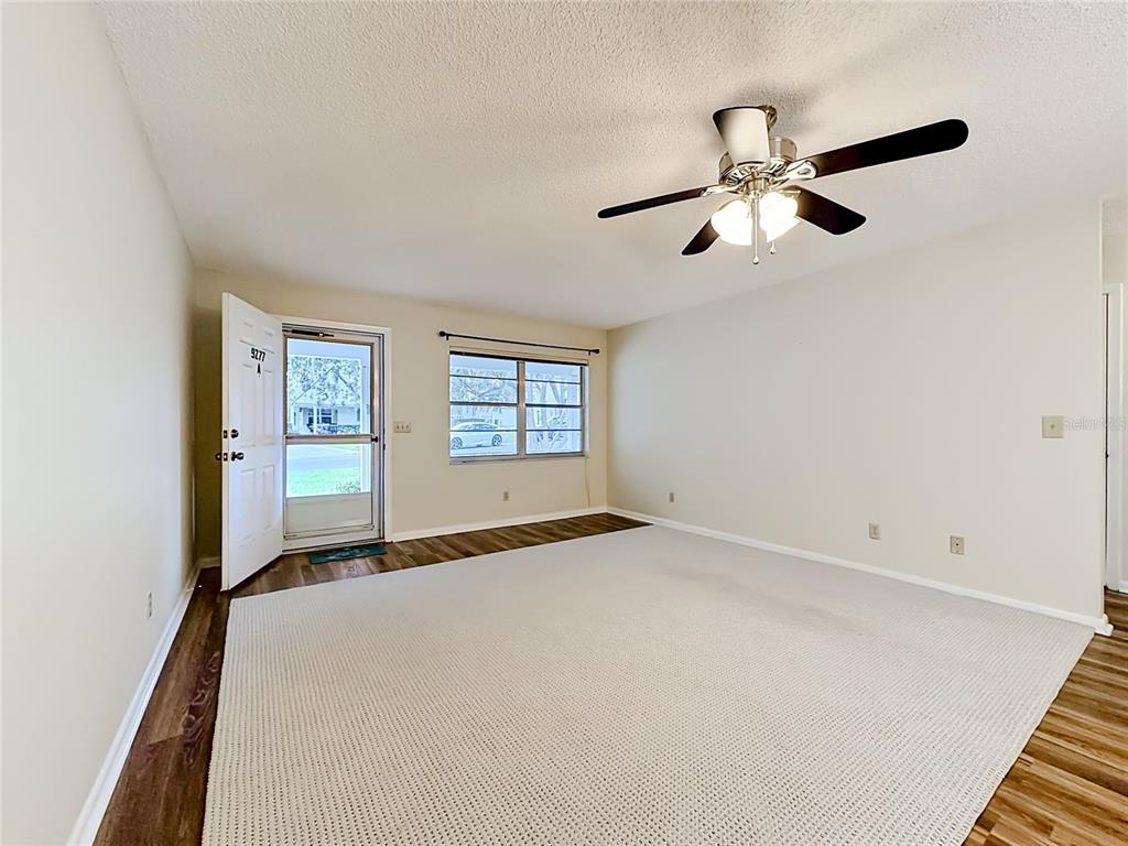 A living room with beige walls, a ceiling fan, carpeted flooring, and an open front door — 9277 SW 83RD AVENUE UNIT A, OCALA, FL