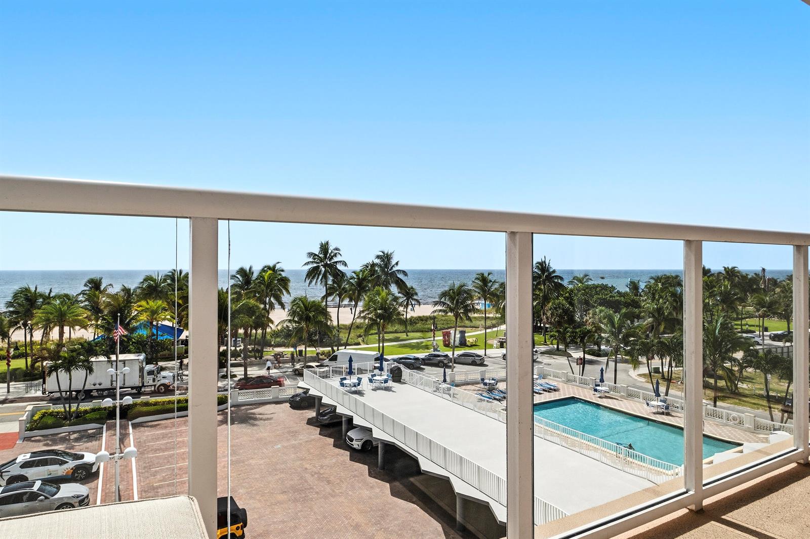 A balcony view overlooks a parking lot, a swimming pool, palm trees, and the ocean — 111 N Pompano Beach Boulevard # 611, Pompano Beach FL 33062, POMPANO BEACH, FL