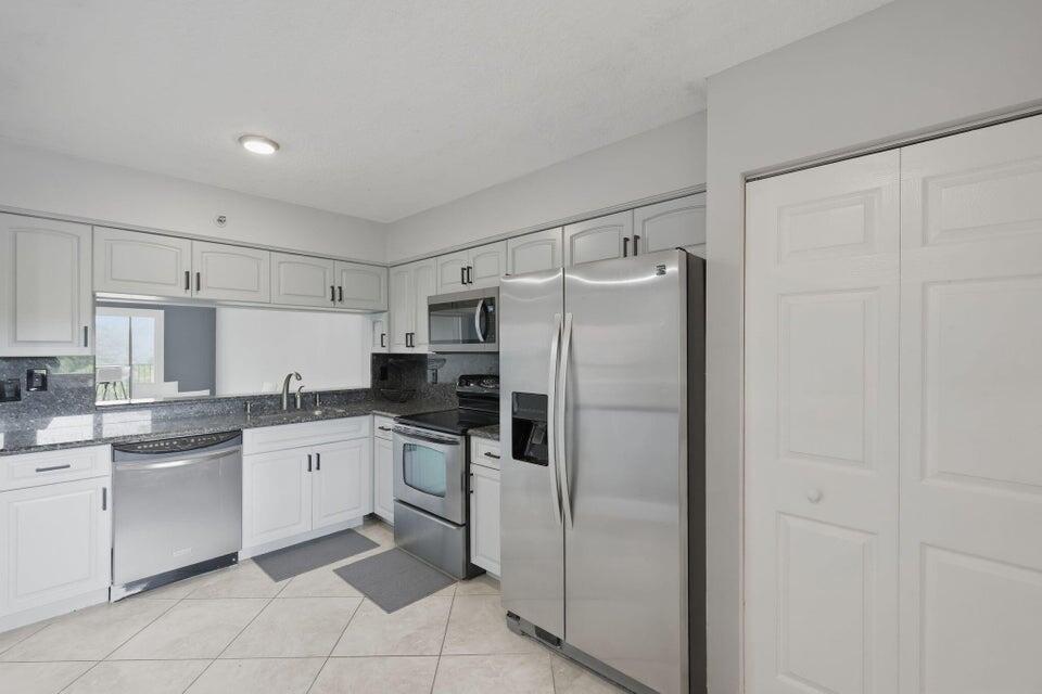 A kitchen with white cabinets, stainless steel appliances, granite countertops, and light-colored tile flooring — 2206 S Cypress Bend Drive # 401, Pompano Beach FL 33069, POMPANO BEACH, FL