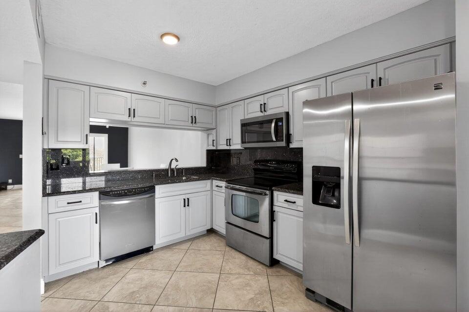 A kitchen with light gray cabinets, stainless steel appliances, dark countertops, and tile flooring — 2206 S Cypress Bend Drive # 401, Pompano Beach FL 33069, POMPANO BEACH, FL