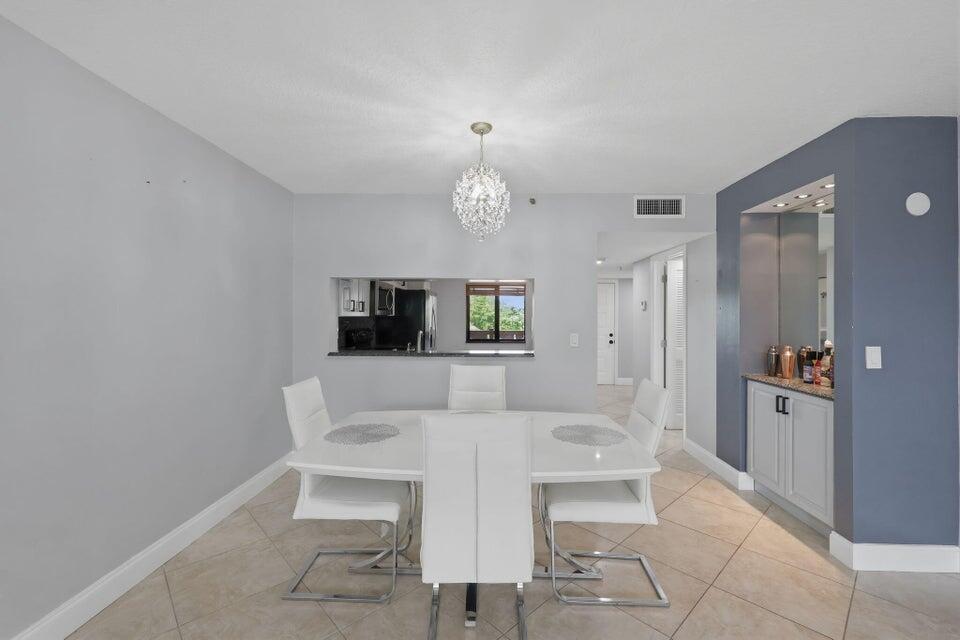 A dining room with a white table, modern chairs, a chandelier, and a built-in bar — 2206 S Cypress Bend Drive # 401, Pompano Beach FL 33069, POMPANO BEACH, FL