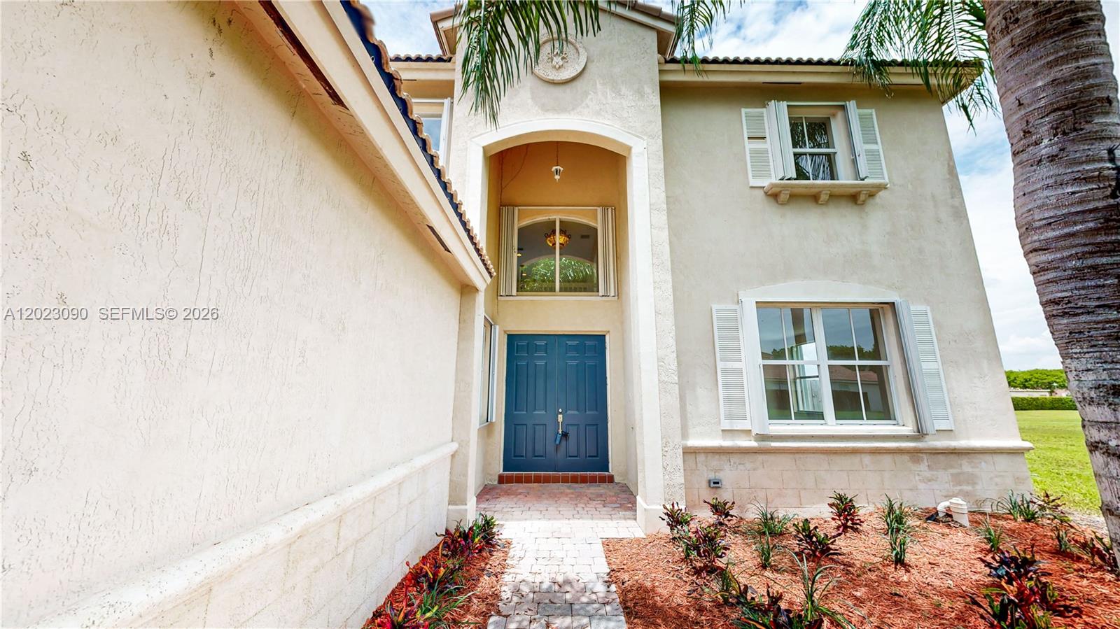 The exterior of a two-story stucco house features a blue double-door entrance and landscaping — 1730 SE 20th Ter, Homestead FL 33035, HOMESTEAD, FL