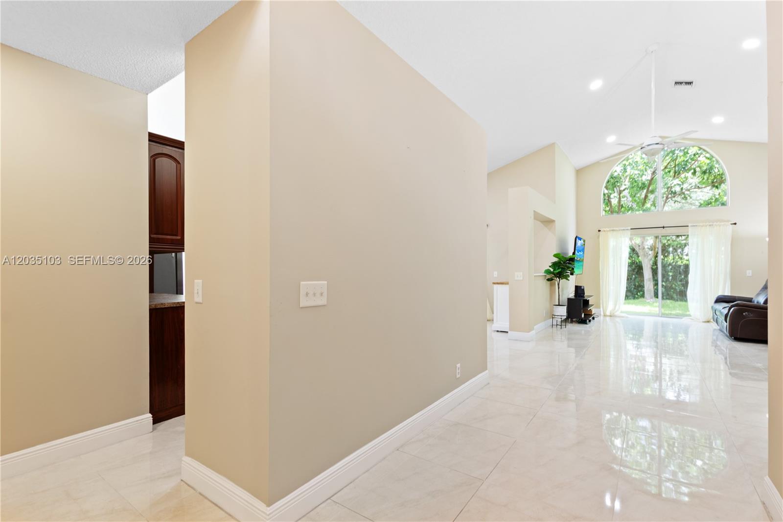 A bright, open-concept living area features beige walls, white tile flooring, and a large arched window — 11637 NW 3rd Dr, Coral Springs FL 33071, CORAL SPRINGS, FL