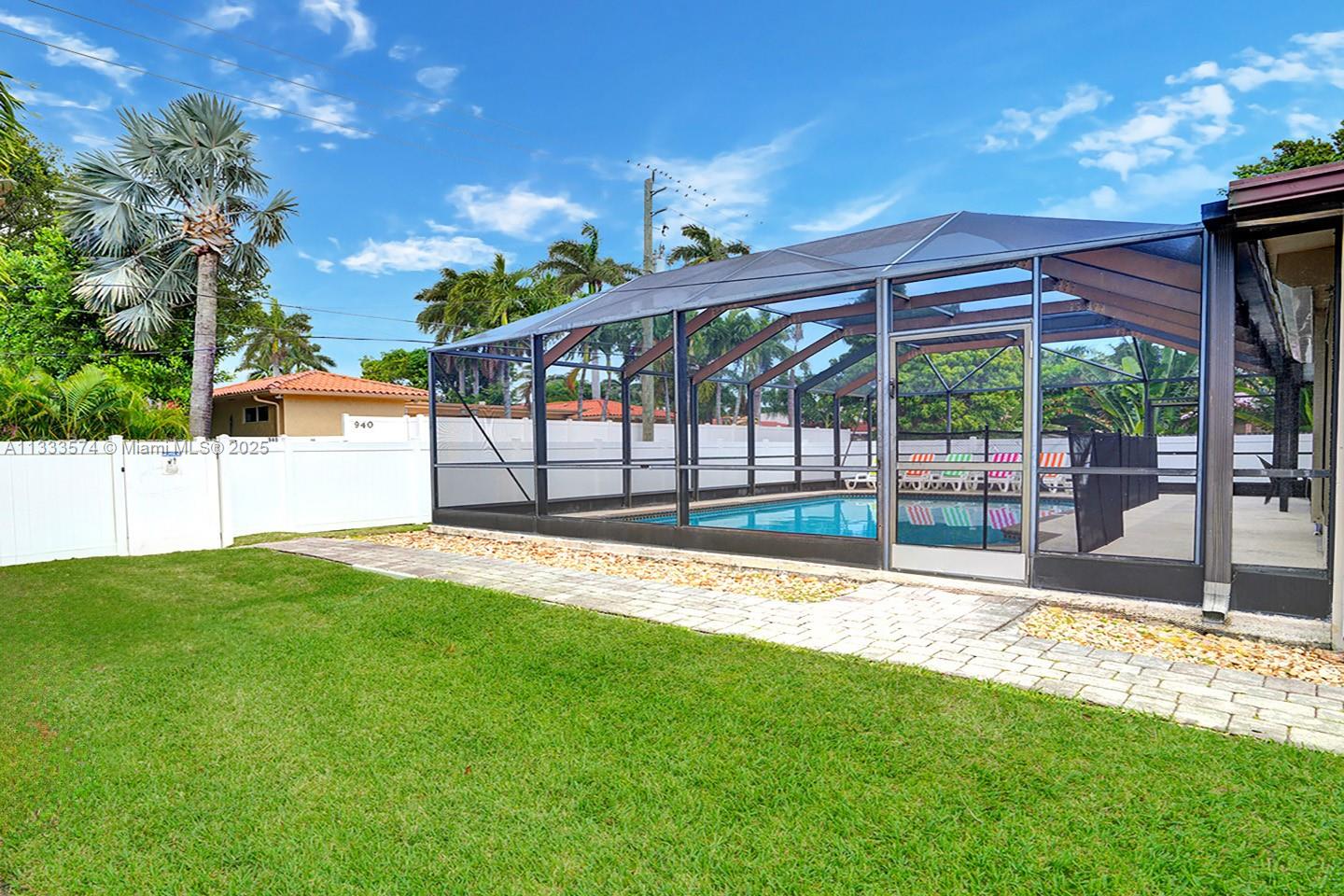 A backyard features a swimming pool enclosed by a screened lanai next to a grassy lawn — 947 Washington St, Hollywood FL 33019, HOLLYWOOD, FL