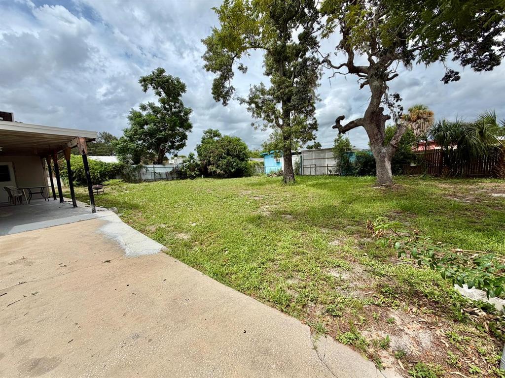 A concrete patio overlooks a grassy backyard with mature trees and a fenced perimeter — 7215 JAMES STREET, PORT RICHEY, FL