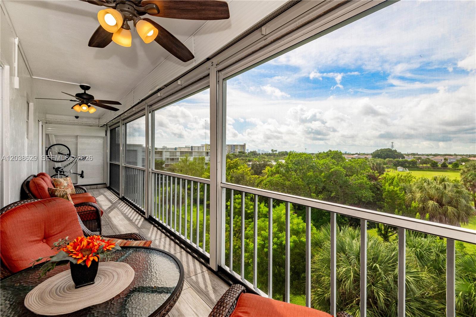 A screened-in balcony features wicker furniture, ceiling fans, and a view of trees and buildings — 4800 Hillcrest Ln # 501, Hollywood FL 33021, HOLLYWOOD, FL