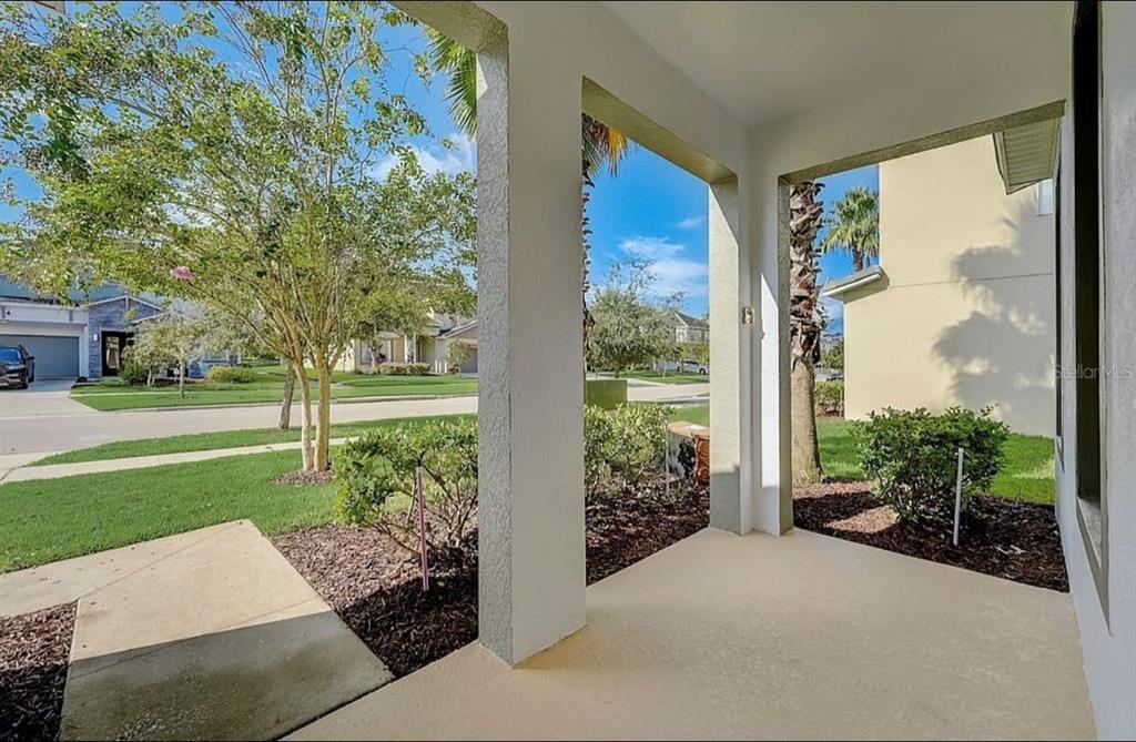 A covered front porch with concrete flooring overlooks a suburban street and neighborhood landscaping — 4511 MONADO DRIVE, KISSIMMEE, FL