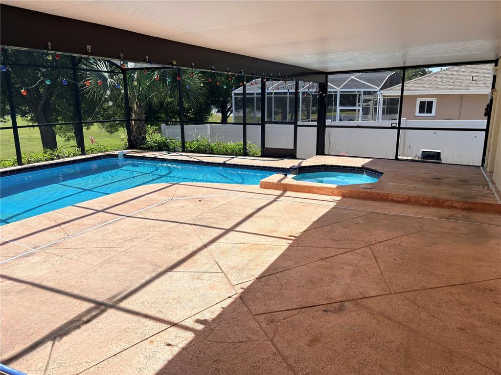 A screened-in pool enclosure features a concrete deck, a swimming pool, and a small spa — 1105 INDIAN RIDGE TRAIL E, KISSIMMEE, FL