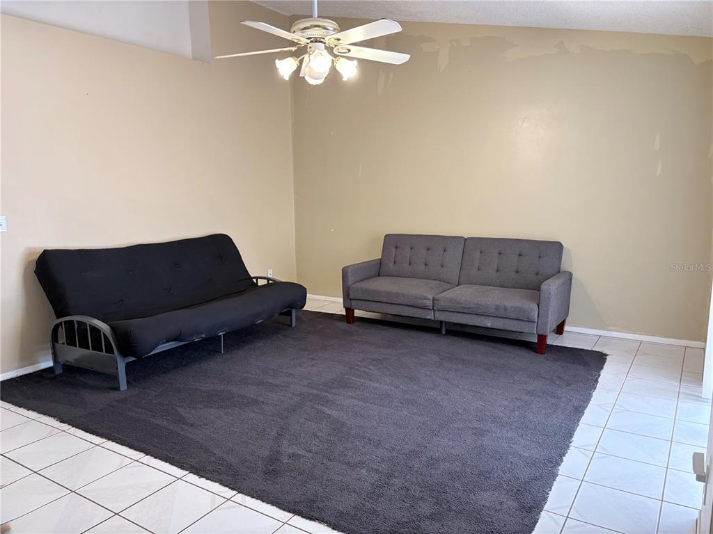 A living room features a black futon, a gray sofa, and a dark area rug — 1105 INDIAN RIDGE TRAIL E, KISSIMMEE, FL