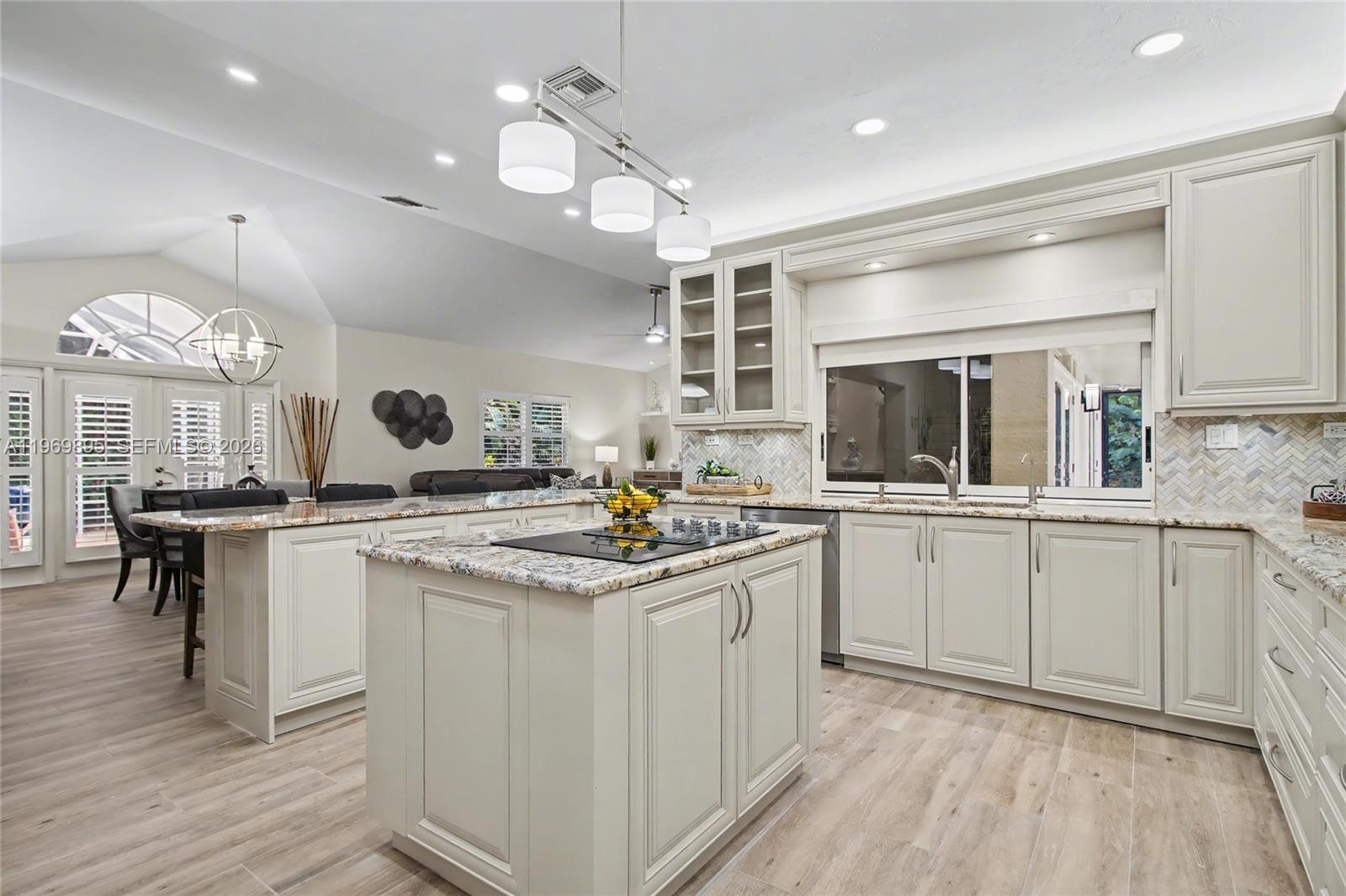 A kitchen features light-colored cabinetry, granite countertops, a central island, and wood-look tile flooring — 5186 Tallowood Way, Naples FL 34116, NAPLES, FL