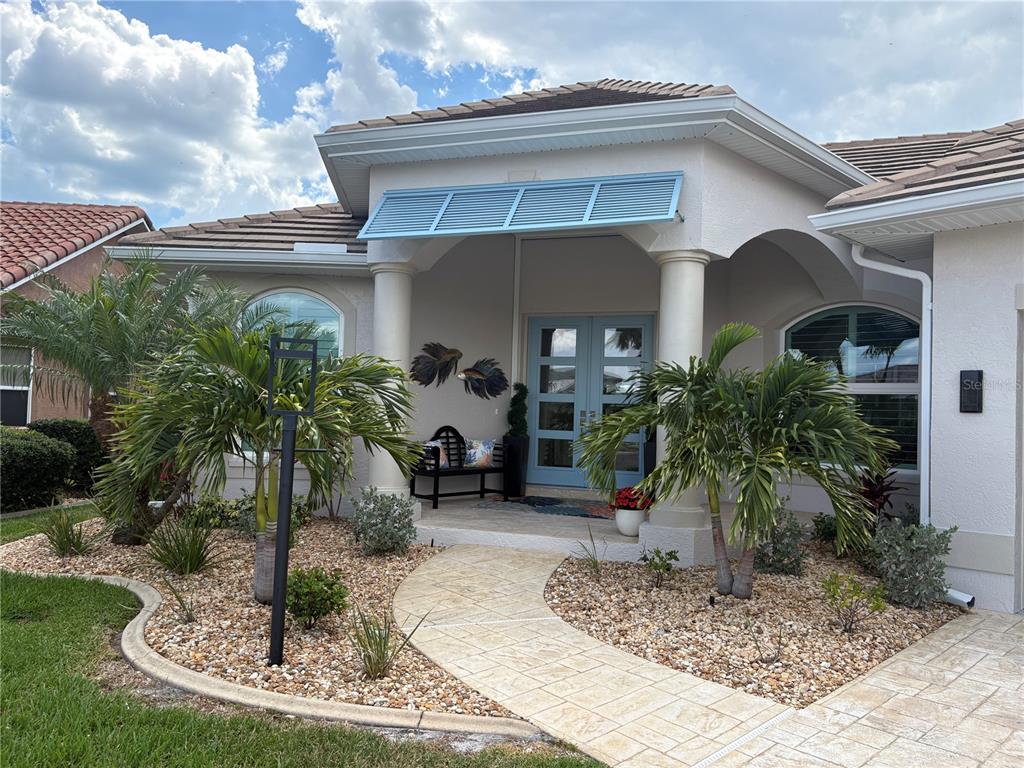 A light-colored house exterior features a blue front door, matching shutters, and palm trees — 136 GREAT ISAAC COURT, PUNTA GORDA, FL