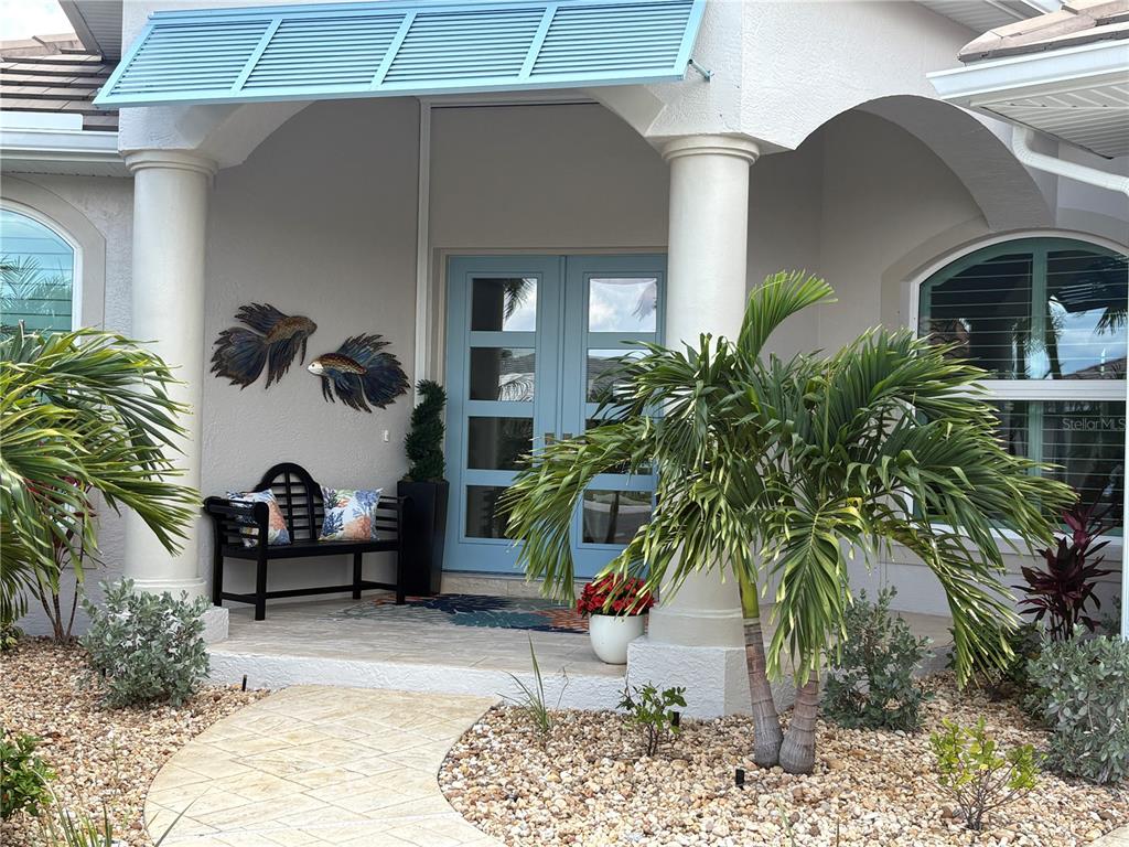 The exterior entrance features a light blue double door, a black bench, and palm trees — 136 GREAT ISAAC COURT, PUNTA GORDA, FL