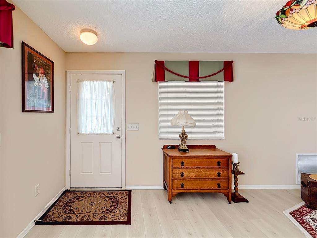 A foyer features light wood-look flooring, a white front door, and a wooden chest — 3598 CAMBRIA CIRCLE, THE VILLAGES, FL