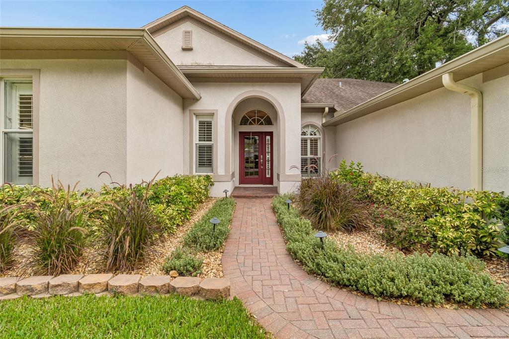 A brick walkway leads to the arched front entrance of a beige stucco house — 3825 MISTY LANDING DRIVE, VALRICO, FL