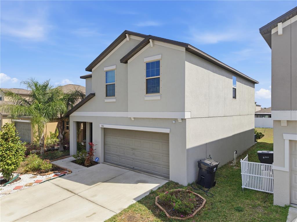 A two-story house with a beige stucco exterior, a two-car garage, and a small yard — 861 OLIVE CONCH STREET, RUSKIN, FL