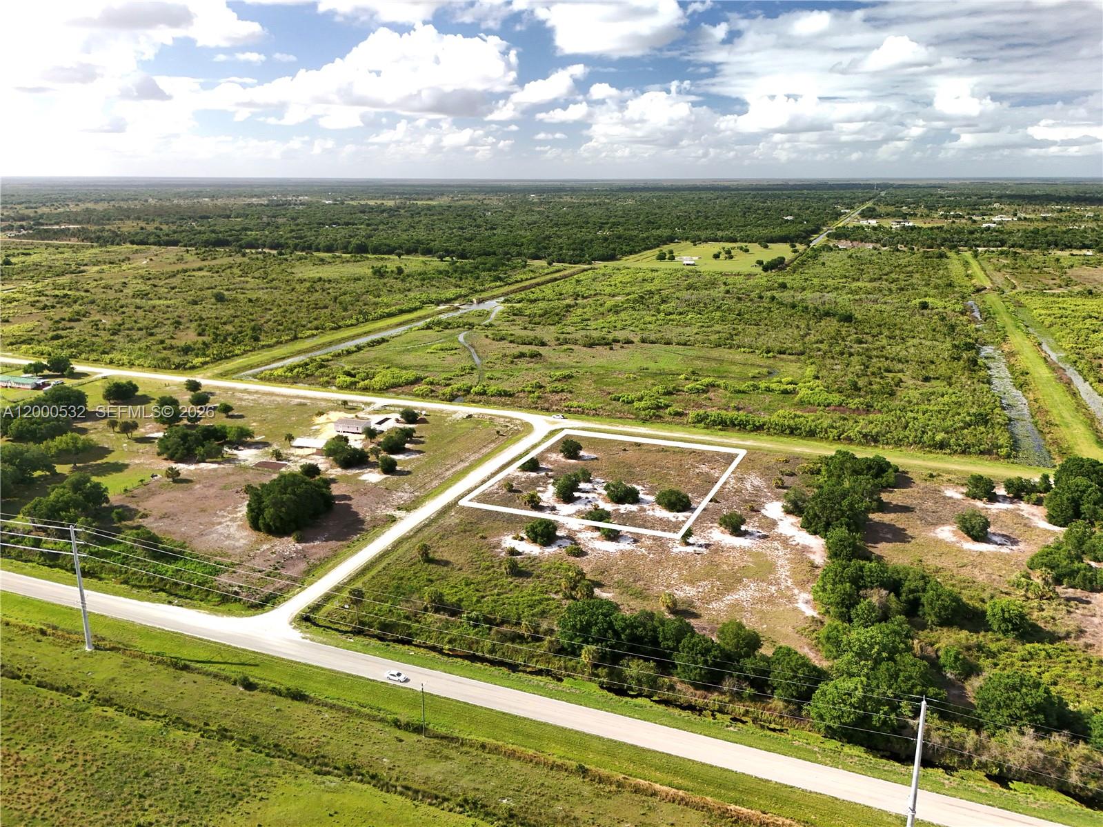 An aerial view shows a vacant, rectangular lot outlined in white near a rural road — 16734 NW 242ND, Okeechobee FL 34972, OKEECHOBEE, FL
