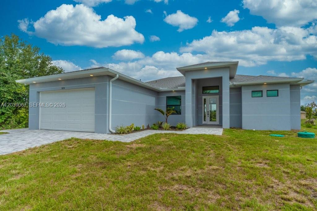 A modern single-story house with a gray exterior, a two-car garage, and a paved walkway — 5054 Benton St, Lehigh Acres FL 33971, LEHIGH ACRES, FL