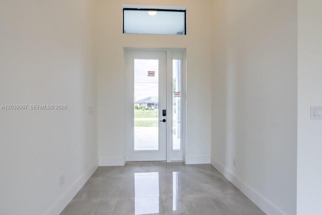 A bright entryway features light gray tile flooring, white walls, and a glass-paneled front door — 5054 Benton St, Lehigh Acres FL 33971, LEHIGH ACRES, FL