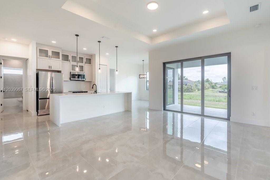 A modern kitchen with white cabinetry and a large island opens to a living area — 5054 Benton St, Lehigh Acres FL 33971, LEHIGH ACRES, FL
