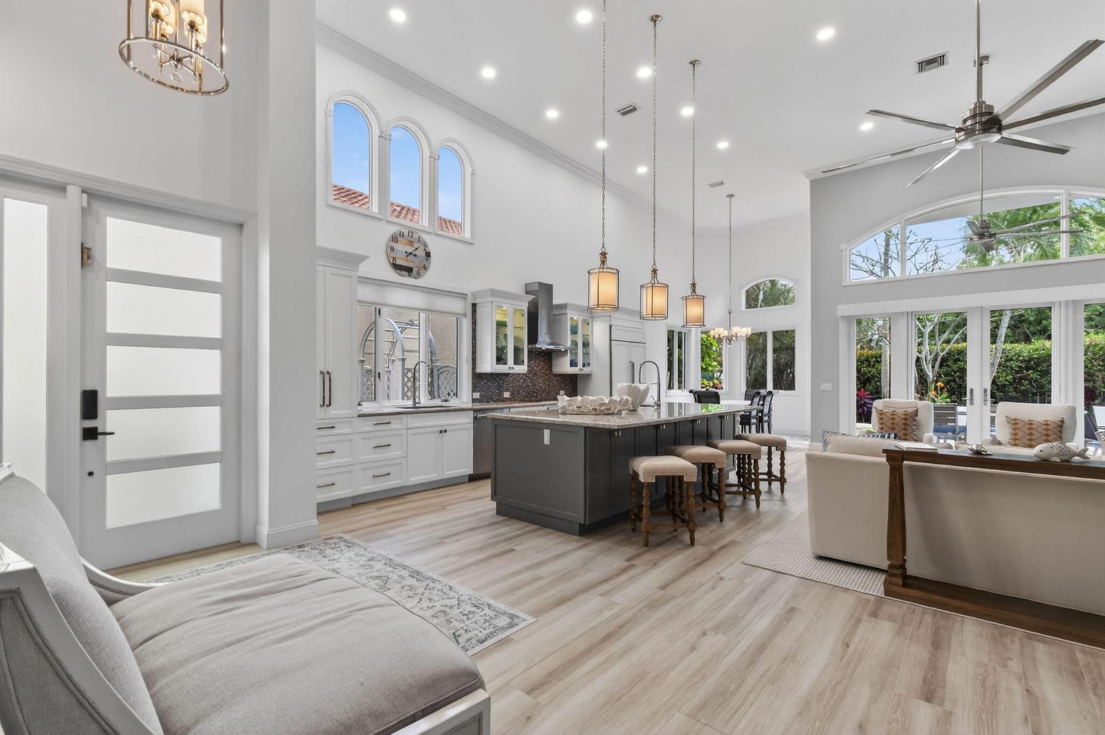 A bright, open-concept kitchen and living area features a large dark island, white cabinetry, and high ceilings — 302 Alicante Drive, Juno Beach FL 33408, JUNO BEACH, FL