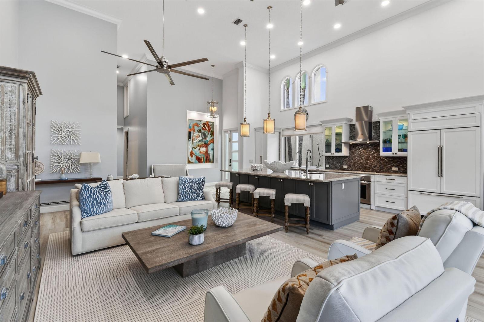 An open-concept living room and kitchen featuring a large island, high ceilings, and neutral decor — 302 Alicante Drive, Juno Beach FL 33408, JUNO BEACH, FL