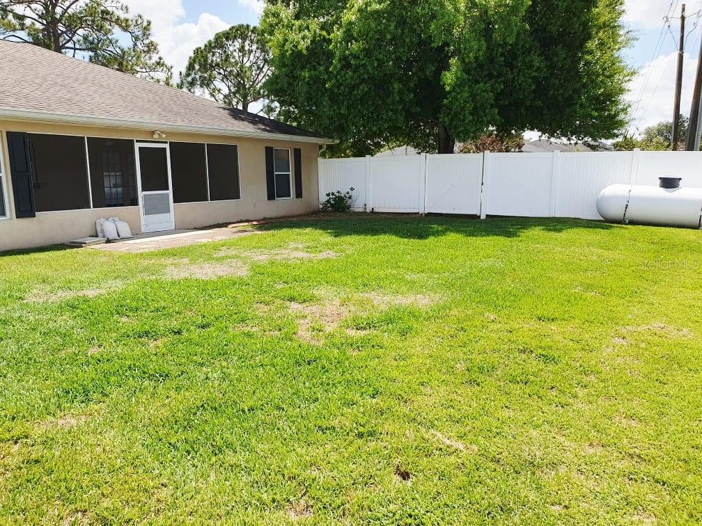 A backyard features a grass lawn, a screened-in patio, and a white vinyl privacy fence — 4031 SANTA BARBARA DRIVE, SEBRING, FL