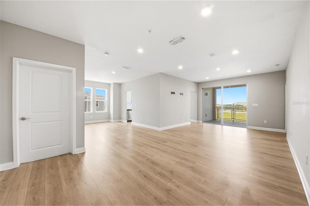 An open-concept living area with light wood-look flooring, recessed lighting, and a sliding glass door — 7521 LAUREATE BOULEVARD UNIT 5403, ORLANDO, FL