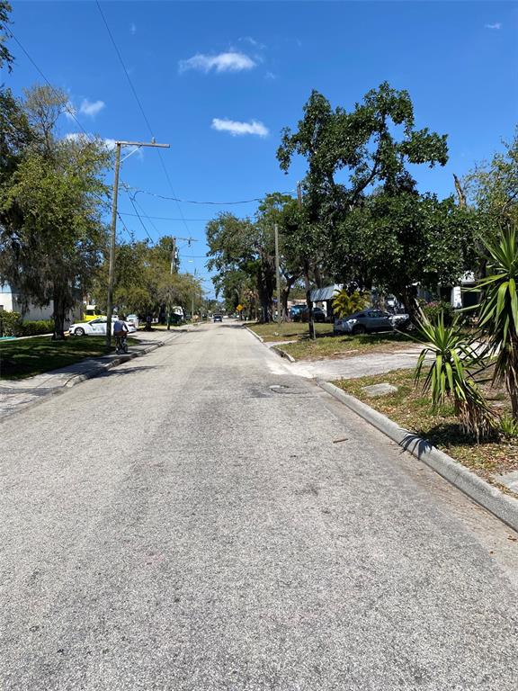A paved residential street lined with trees, utility poles, and parked cars under a blue sky — 518 7TH AVENUE W, PALMETTO, FL