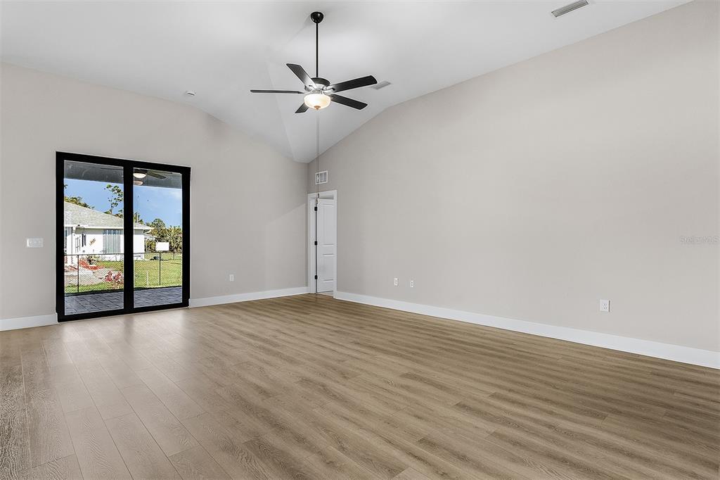 An empty room with light wood-look flooring, a vaulted ceiling, and sliding glass patio doors — 4570 GILLOT BOULEVARD, PORT CHARLOTTE, FL