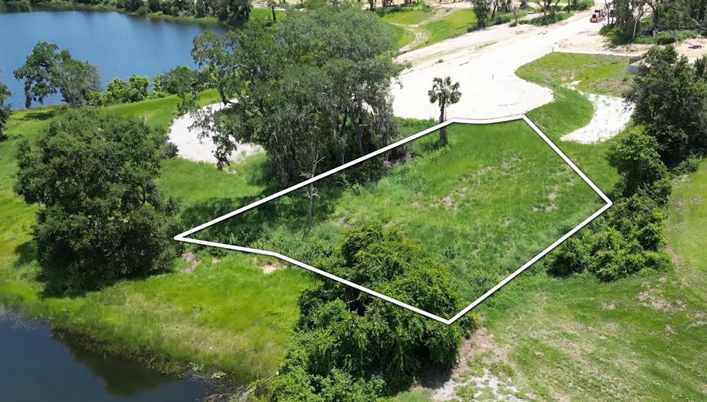 An aerial view shows a vacant, grassy lot outlined in white near a lake — 129 TRANQUIL MIRROR LAKE COURT Lot 17, CLERMONT, FL