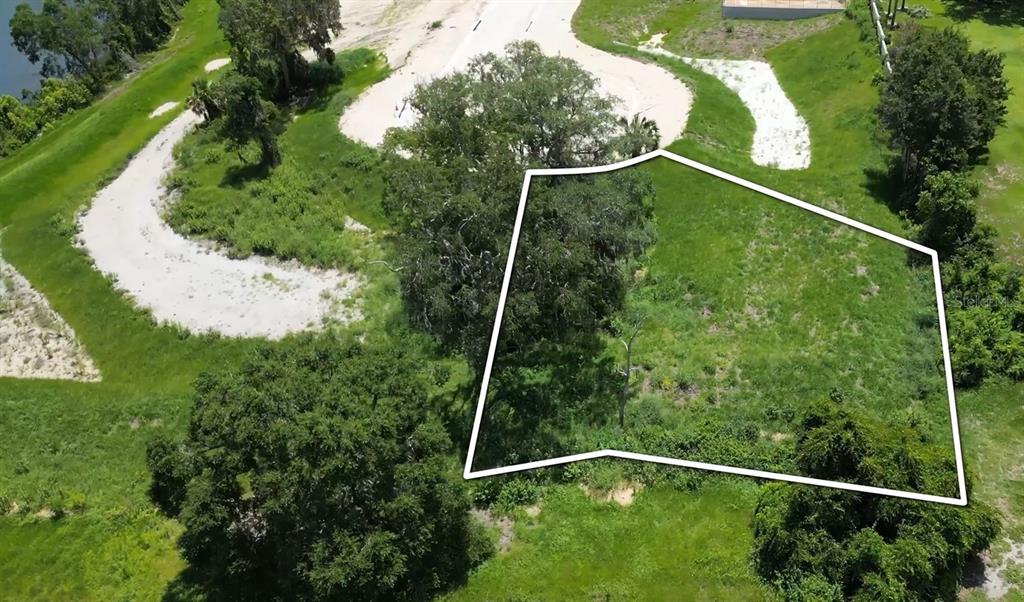 An aerial view shows a grassy, undeveloped lot outlined in white near a paved road — 129 TRANQUIL MIRROR LAKE COURT Lot 17, CLERMONT, FL