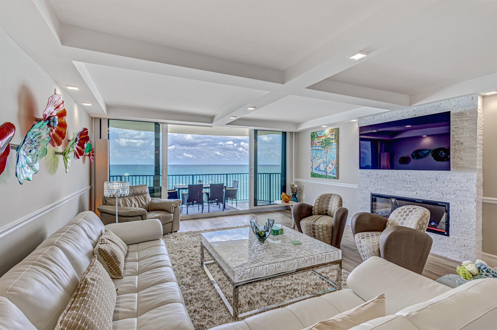 A living room with a white leather sofa, fireplace, and balcony overlooking the ocean — 400 Beach Road # 702, Tequesta FL 33469, TEQUESTA, FL