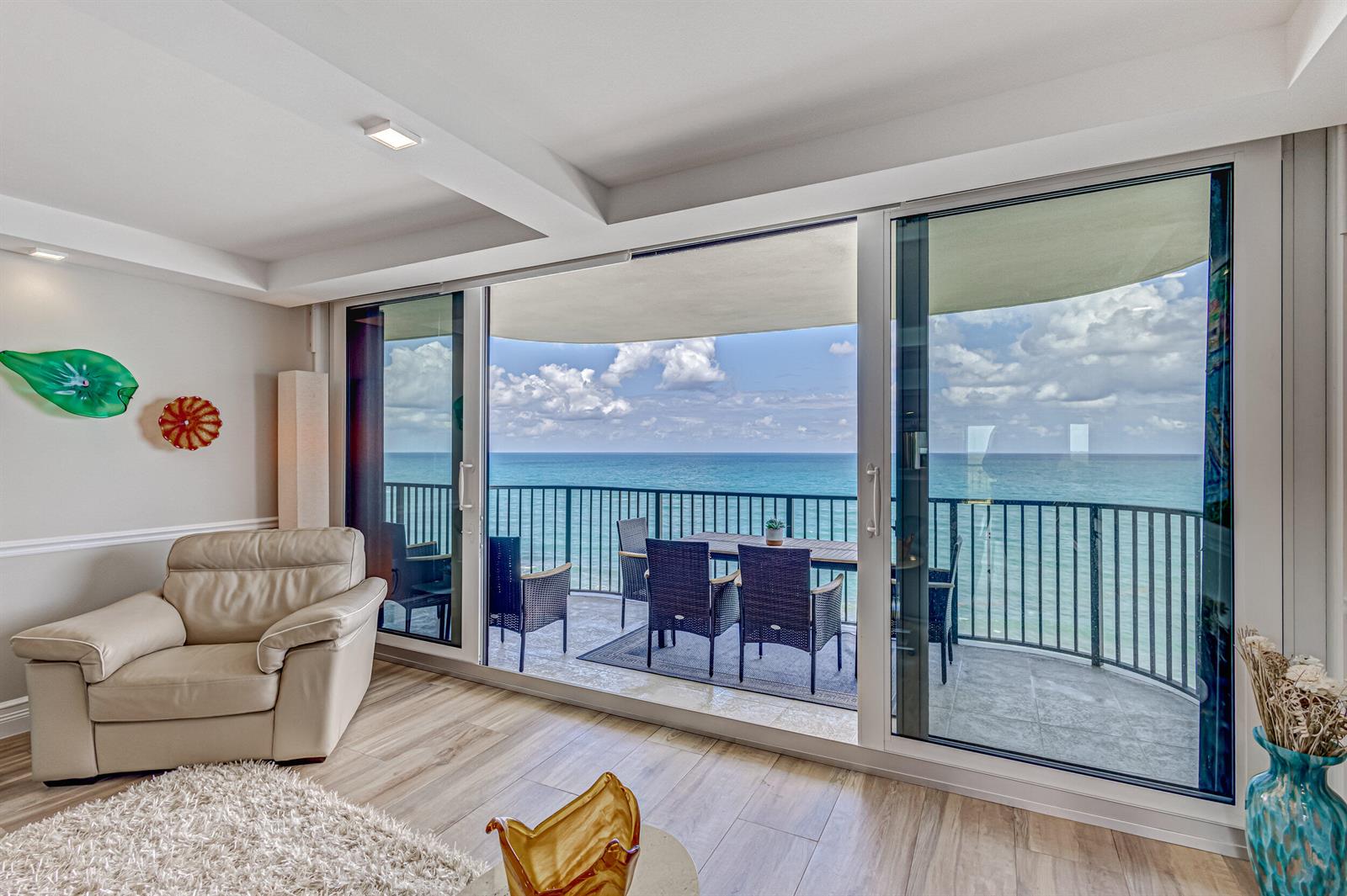 A living room with a leather armchair opens onto a balcony overlooking the ocean — 400 Beach Road # 702, Tequesta FL 33469, TEQUESTA, FL