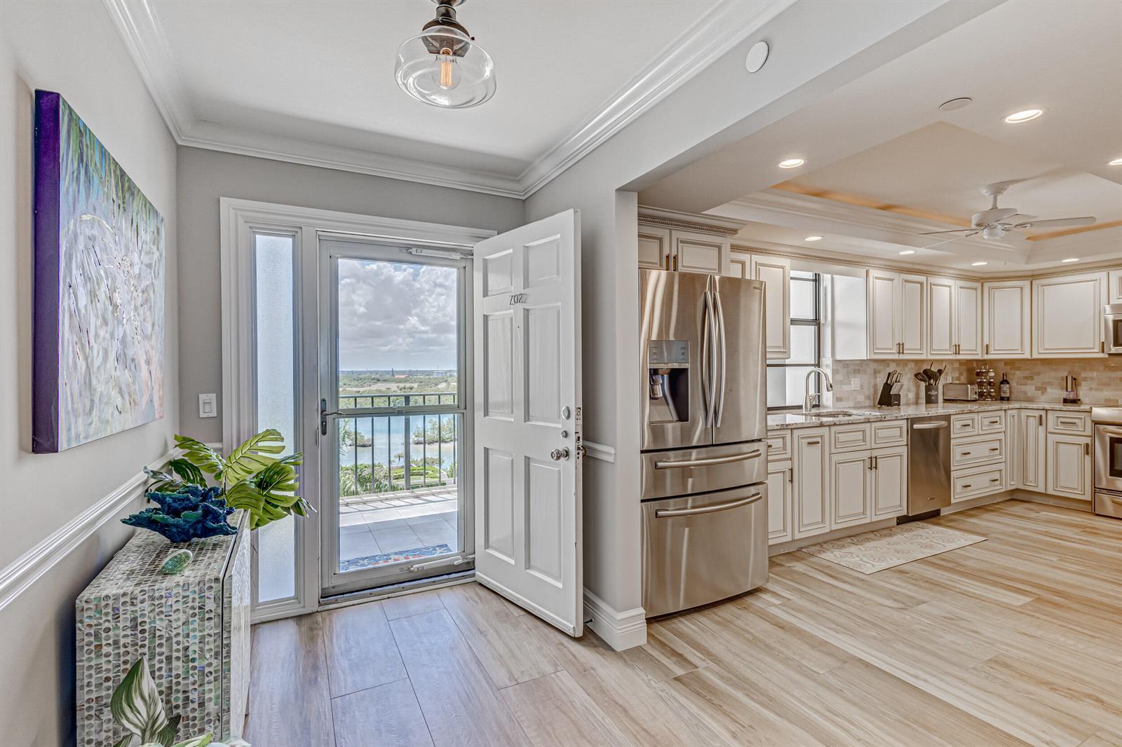 An open-concept kitchen features white cabinetry, stainless steel appliances, and a door leading to a balcony — 400 Beach Road # 702, Tequesta FL 33469, TEQUESTA, FL