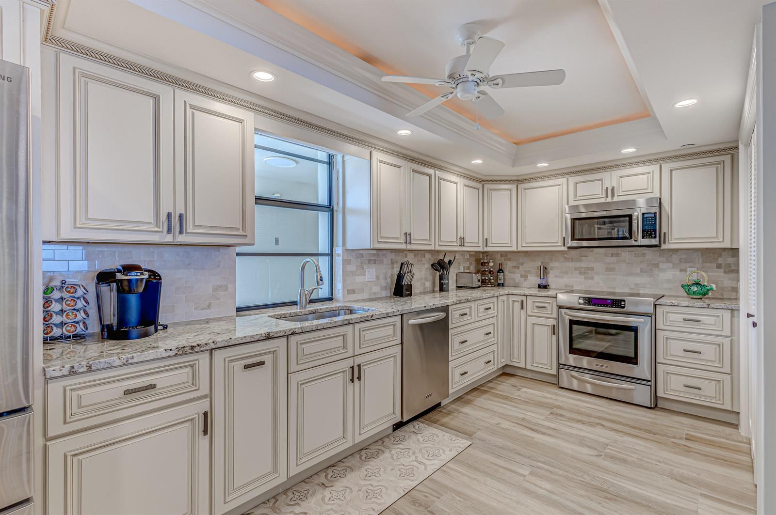 A kitchen features white cabinetry, granite countertops, stainless steel appliances, and light wood-look flooring — 400 Beach Road # 702, Tequesta FL 33469, TEQUESTA, FL