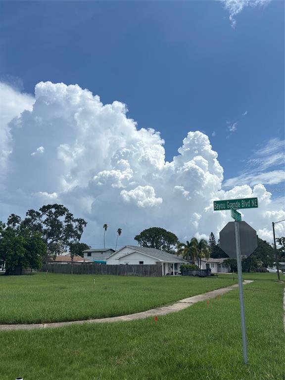 A grassy corner lot with a street sign and houses under a large, cloudy sky — BAYOU GRANDE BOULEVARD NE, ST PETERSBURG, FL