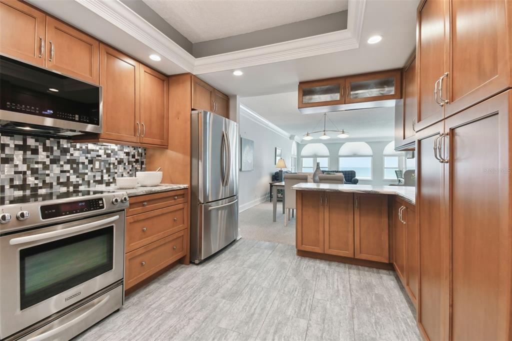 A kitchen with wood cabinets, stainless steel appliances, and a tiled floor opens to a living area — 4950 GULF BOULEVARD UNIT 206, ST PETE BEACH, FL