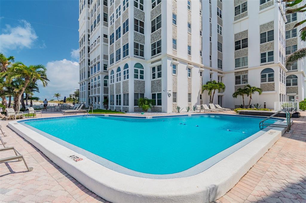 A swimming pool sits in front of a multi-story white building with palm trees — 4950 GULF BOULEVARD UNIT 206, ST PETE BEACH, FL