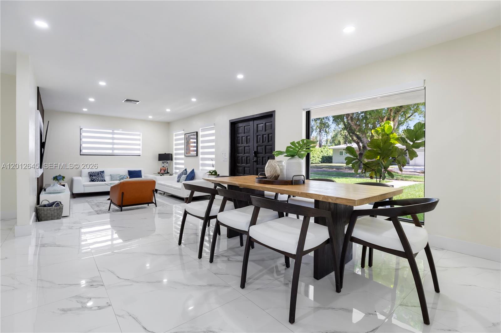 A dining area with a wooden table and white chairs opens into a living room — 1549 Zuleta Ave, Coral Gables FL 33146, CORAL GABLES, FL