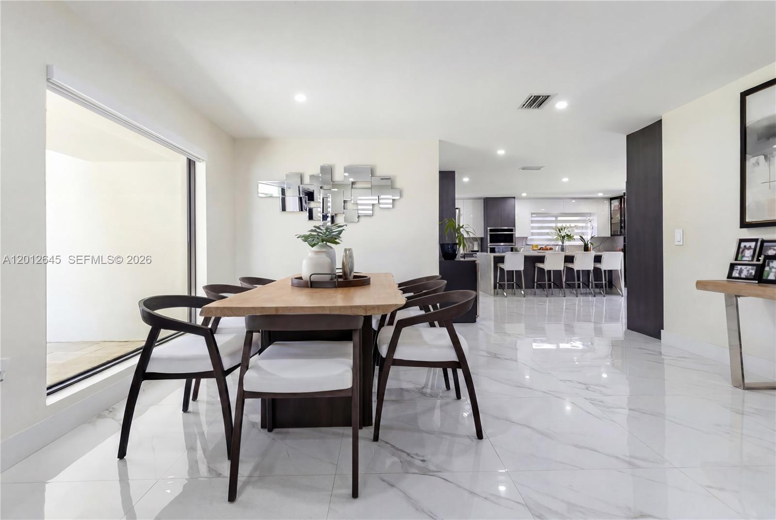 A dining area with a wooden table and chairs sits adjacent to a modern kitchen — 1549 Zuleta Ave, Coral Gables FL 33146, CORAL GABLES, FL
