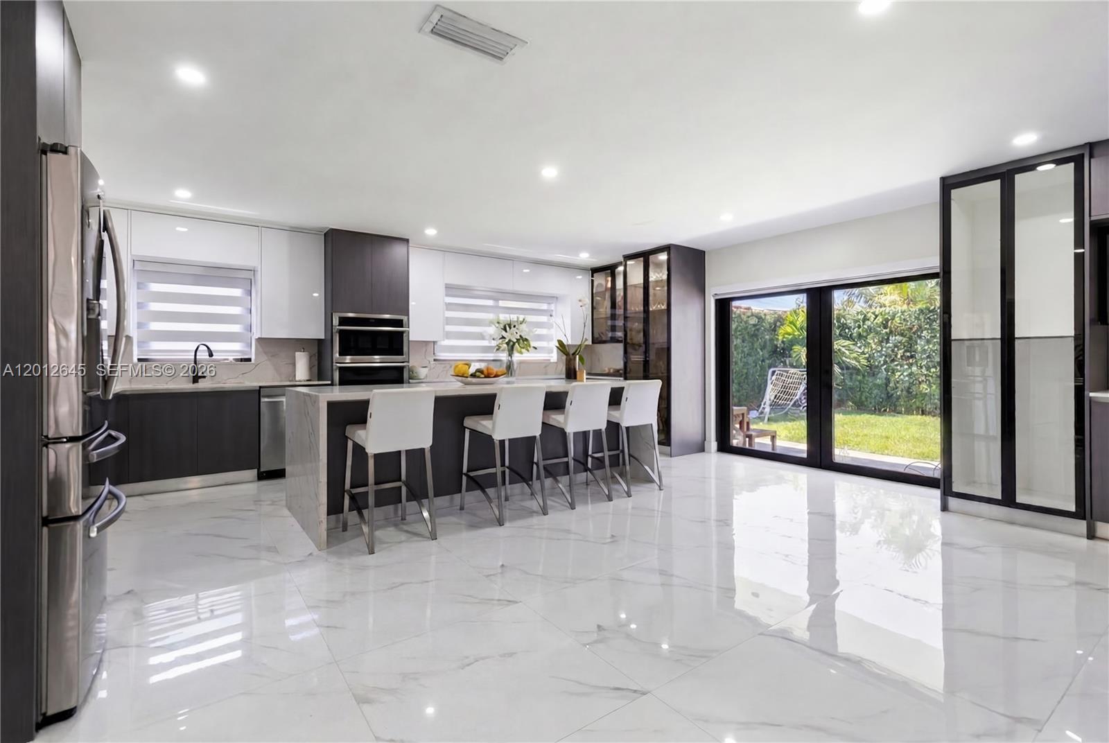 A modern kitchen features white marble floors, dark cabinetry, a large island, and glass doors — 1549 Zuleta Ave, Coral Gables FL 33146, CORAL GABLES, FL