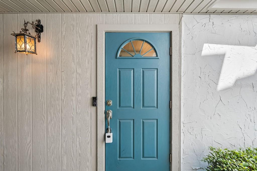 A blue front door with a half-moon window sits between wood-paneled and stucco walls — 500 PARK BOULEVARD S UNIT 24, VENICE, FL