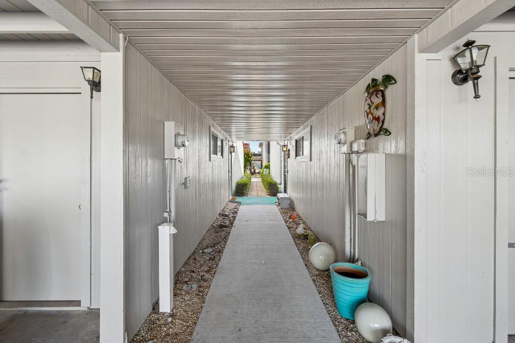 A covered outdoor walkway leads between two buildings toward a sunlit path — 500 PARK BOULEVARD S UNIT 24, VENICE, FL