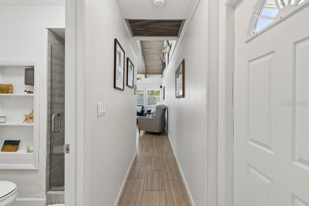 A hallway with wood-look tile flooring leads toward a living area with vaulted ceilings — 500 PARK BOULEVARD S UNIT 24, VENICE, FL