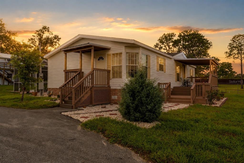 A single-story manufactured home with a wooden porch and deck at sunset — 8020 GRANT STREET, BROOKSVILLE, FL