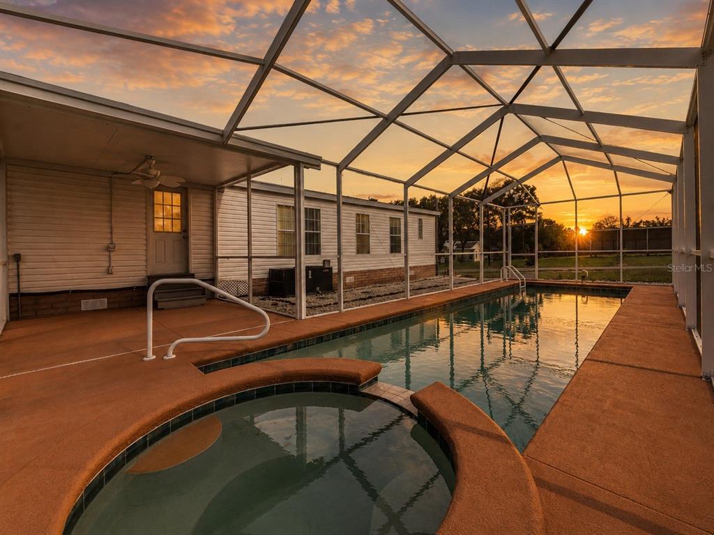 A screened-in pool and spa area with a sunset view behind a residential home — 8020 GRANT STREET, BROOKSVILLE, FL