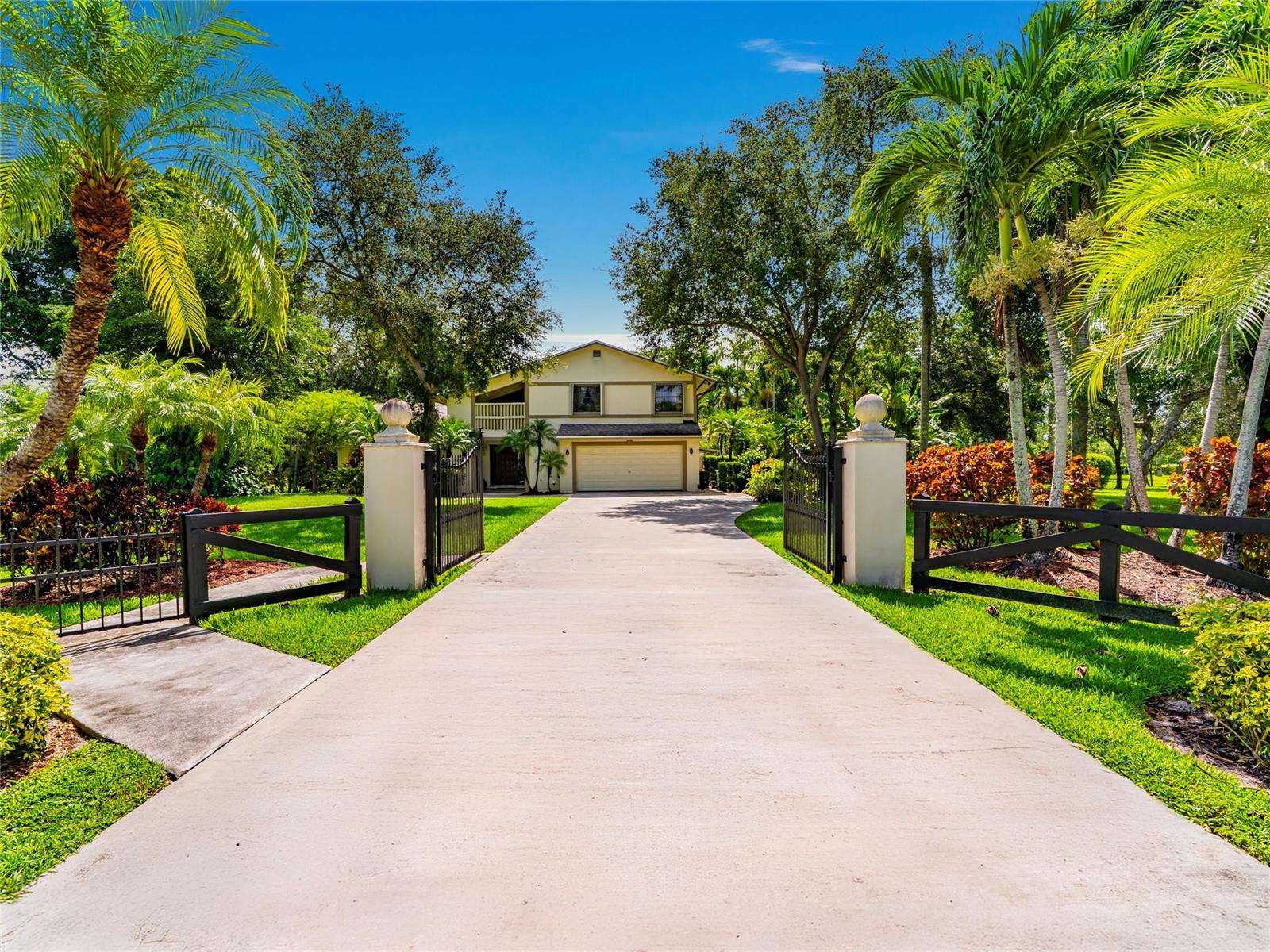 A concrete driveway leads through an open gate to a two-story house with palm trees — 6556 NW 87th Avenue, Parkland FL 33067, PARKLAND, FL
